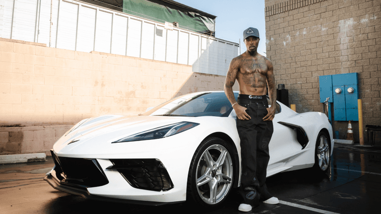 "Amazin Jackson standing next to a white Corvette, showcasing his resilience and entrepreneurial spirit in a powerful moment of confidence."