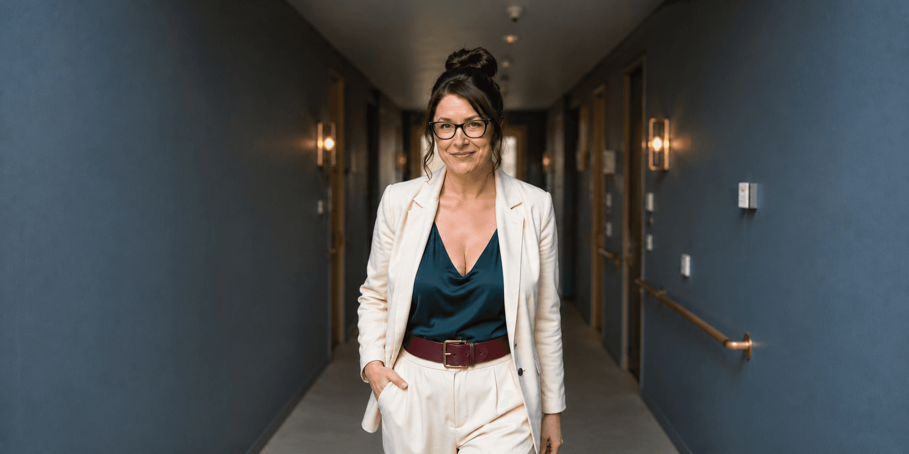 A confident woman in a white suit walking down a stylish hotel corridor