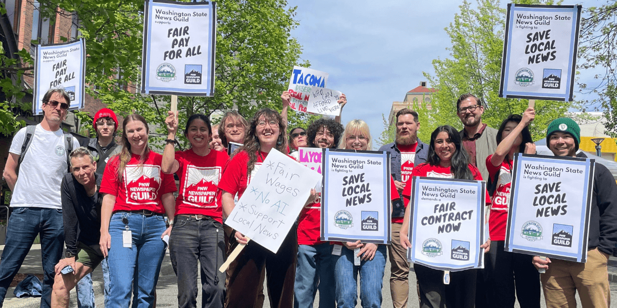 Group of protesters holding signs advocating for fair pay and local news support