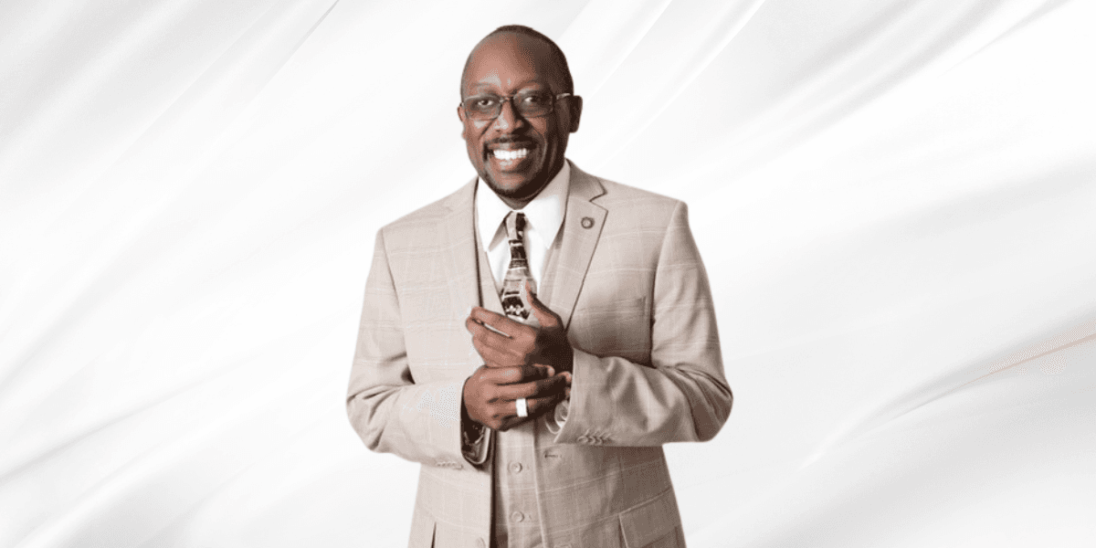 Smiling man in a beige suit holding a small object against a white backdrop