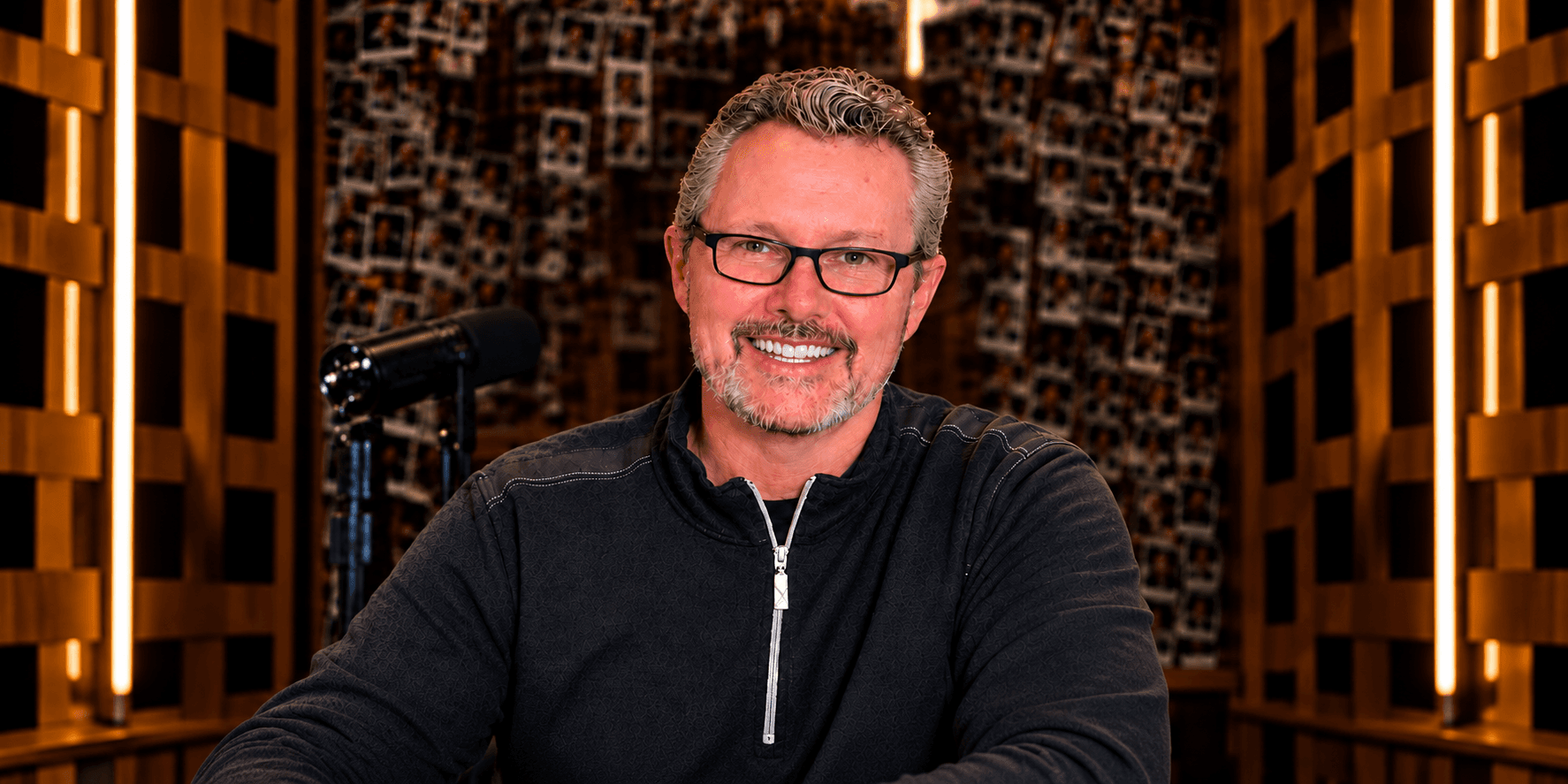 Man with glasses smiling at a desk in a well-lit studio environment