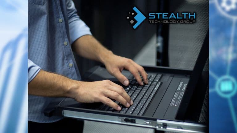 A person typing on a laptop in a server room, showcasing cybersecurity expertise for Stealth Technology Group.