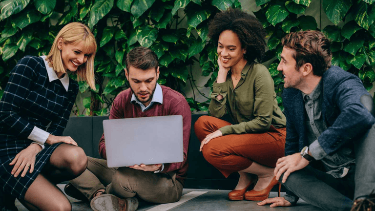 A diverse group of professionals collaborating on a laptop in a modern office setting.