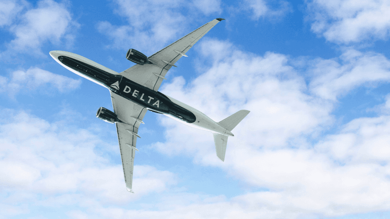Delta Air Lines aircraft flying overhead against a blue sky with scattered clouds.