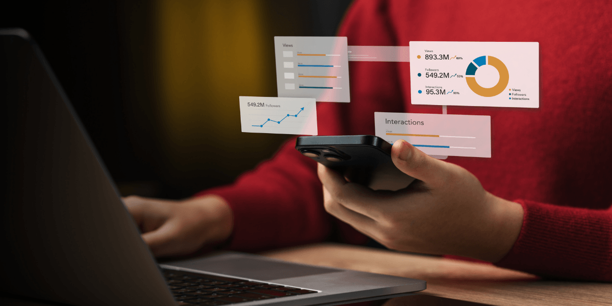 Person holding a smartphone while viewing analytics graphs on a laptop screen
