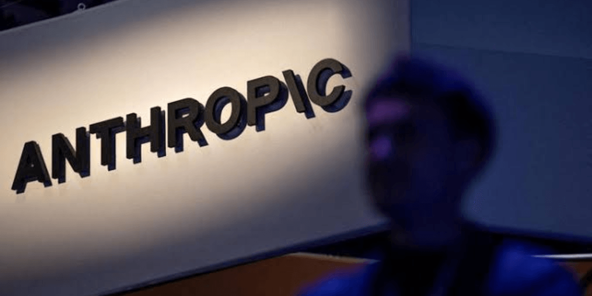 Sign for Anthropic illuminated with a blurred silhouette of a person in the foreground