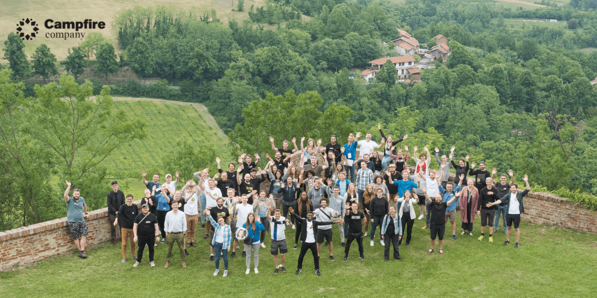 Large group of people outdoors waving, with green hills and buildings in background