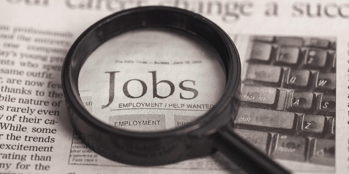 Magnifying glass over a newspaper with the word "Jobs" highlighted prominently
