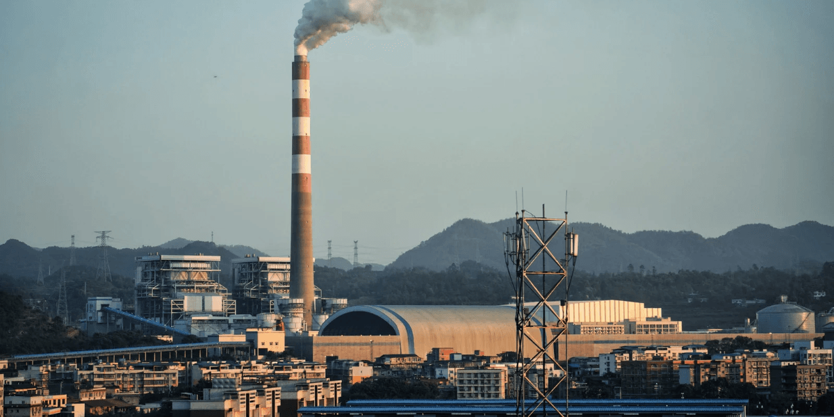 Industrial landscape featuring a smokestack, power plant, and mountainous backdrop.