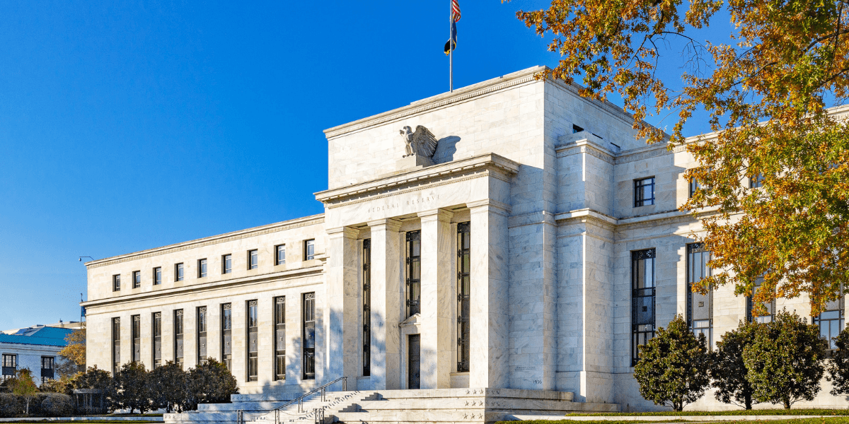 Exterior of a large, neoclassical building with a flag and clear blue sky