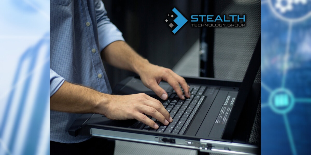 A person typing on a laptop in a server room, showcasing cybersecurity expertise for Stealth Technology Group.