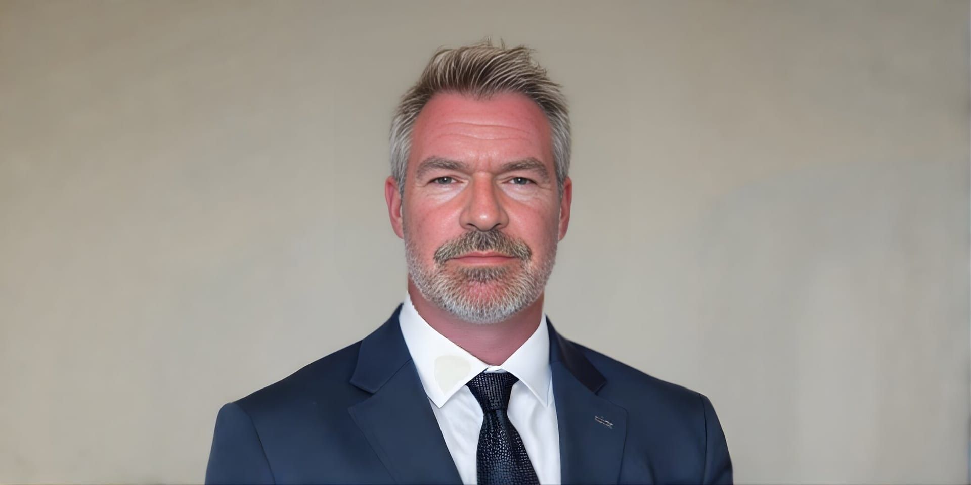 Portrait of Jason Butcher in a navy suit and tie against a neutral background.