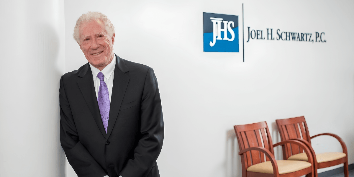 Joel H. Schwartz standing in the firm's Boston office beside the Joel H. Schwartz, P.C. sign.