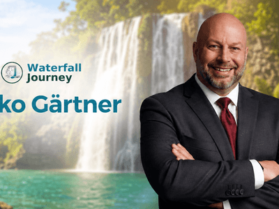 Man in a suit smiling against a scenic waterfall background with text overlay