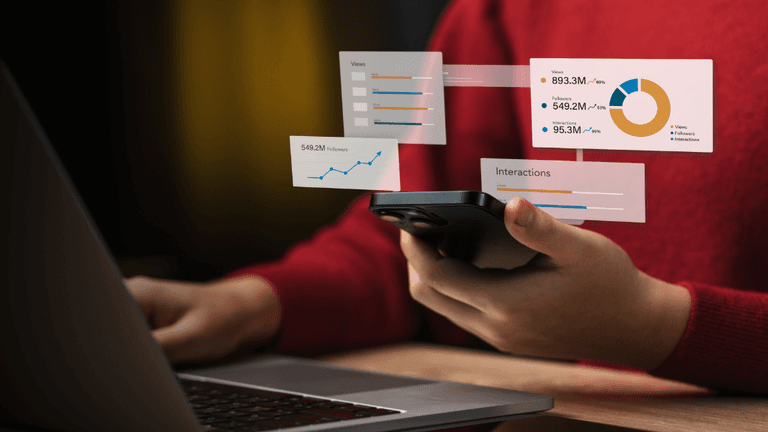 Person holding a smartphone while viewing analytics graphs on a laptop screen