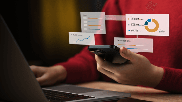 Person holding a smartphone while viewing analytics graphs on a laptop screen