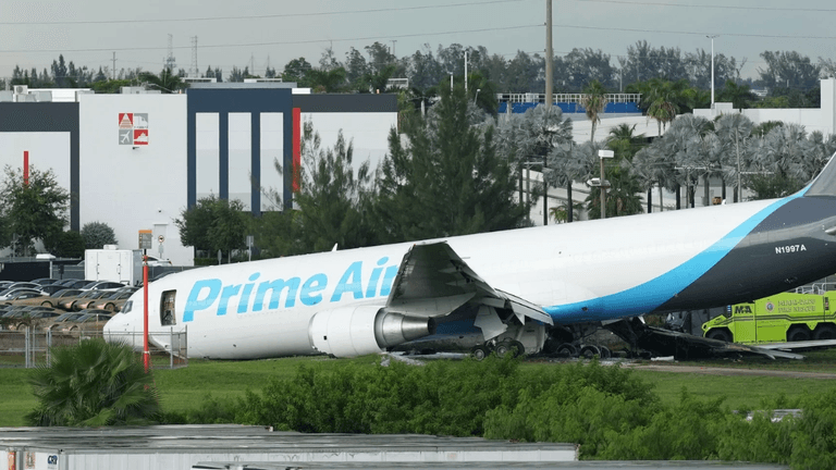 A Prime Air cargo plane is damaged and partially crashed on a grassy area