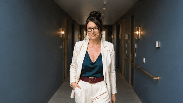 A confident woman in a white suit walking down a stylish hotel corridor