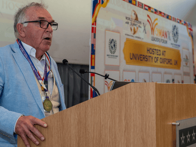 An older man speaks at a podium during a university event or conference