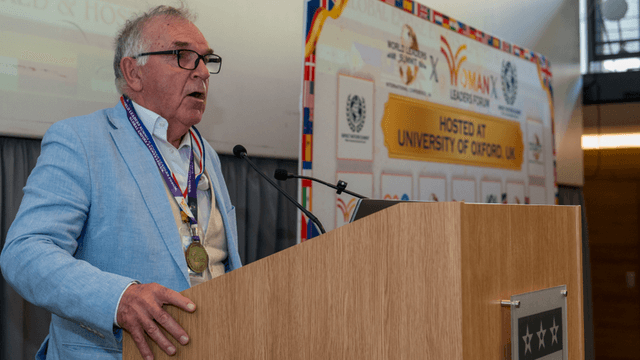 An older man speaks at a podium during a university event or conference
