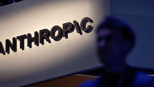 Sign for Anthropic illuminated with a blurred silhouette of a person in the foreground