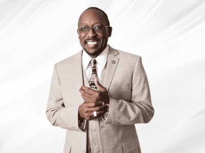 Smiling man in a beige suit holding a small object against a white backdrop