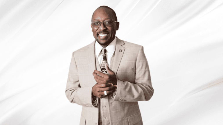 Smiling man in a beige suit holding a small object against a white backdrop