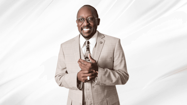 Smiling man in a beige suit holding a small object against a white backdrop