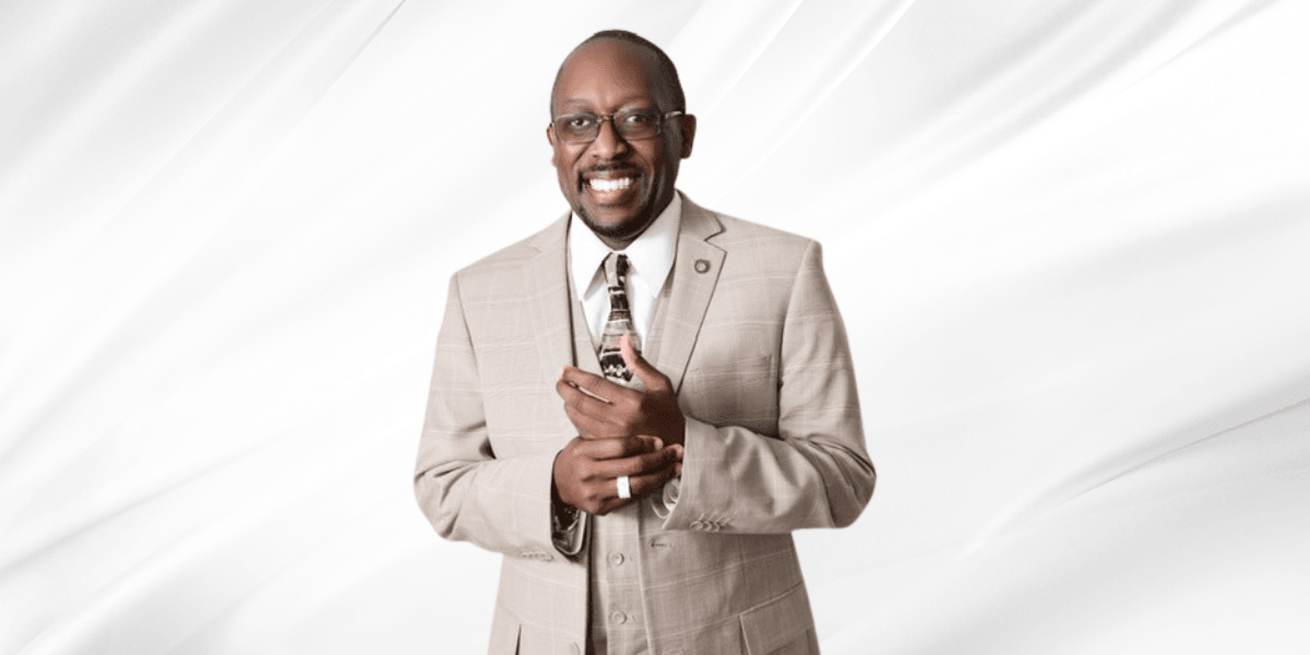 Smiling man in a beige suit holding a small object against a white backdrop