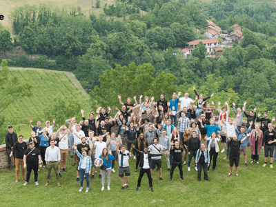 Large group of people outdoors waving, with green hills and buildings in background