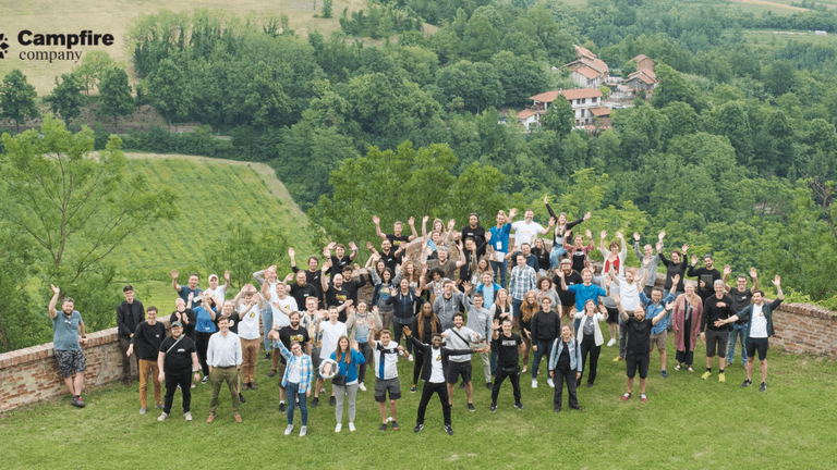 Large group of people outdoors waving, with green hills and buildings in background