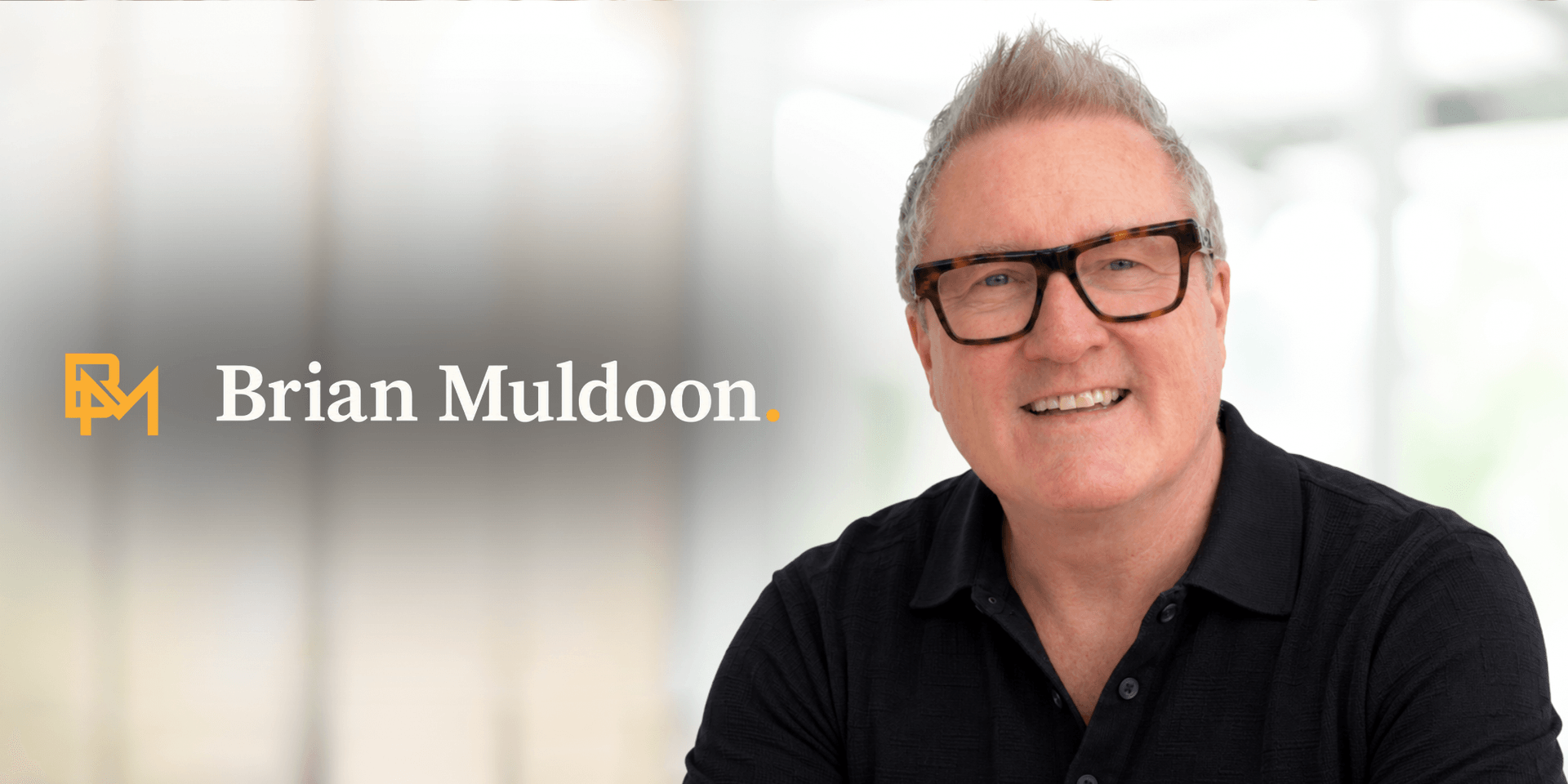 Smiling man with glasses wearing a black shirt, logo displayed beside him