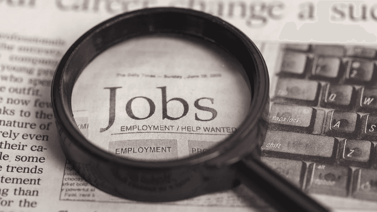 Magnifying glass over a newspaper with the word "Jobs" highlighted prominently