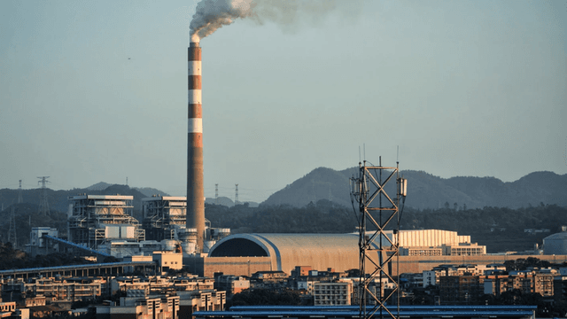 Industrial landscape featuring a smokestack, power plant, and mountainous backdrop.