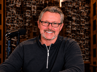 Man with glasses smiling at a desk in a well-lit studio environment
