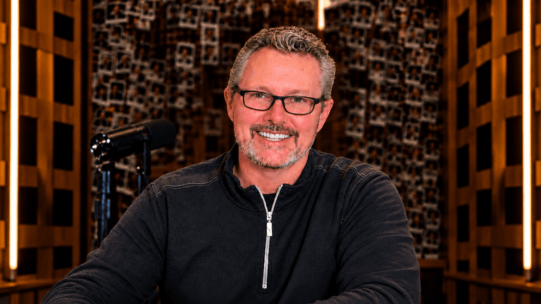 Man with glasses smiling at a desk in a well-lit studio environment