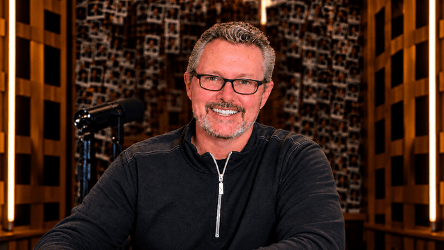 Man with glasses smiling at a desk in a well-lit studio environment