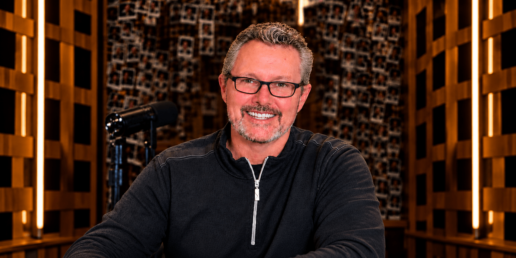 Man with glasses smiling at a desk in a well-lit studio environment