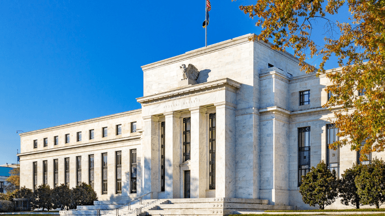 Exterior of a large, neoclassical building with a flag and clear blue sky