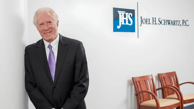 Joel H. Schwartz standing in the firm's Boston office beside the Joel H. Schwartz, P.C. sign.