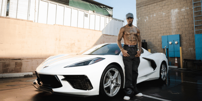 "Amazin Jackson standing next to a white Corvette, showcasing his resilience and entrepreneurial spirit in a powerful moment of confidence."