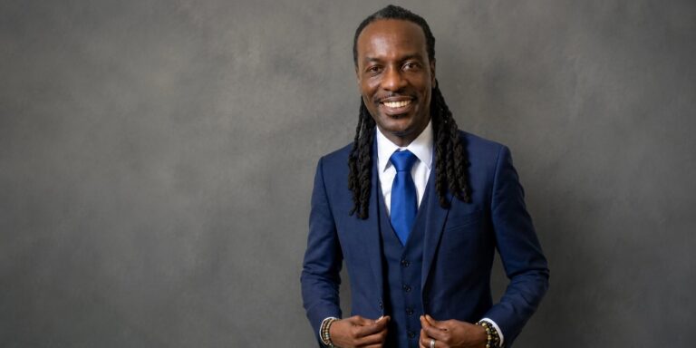 Formal portrait of author Cleous G. Young smiling in a blue suit against a gray backdrop.