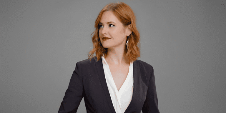 The Girl On The Left Returns: Megan Dirks on Why the Story Never Ends at One Book Red-haired woman wearing a dark blazer and white blouse against a gray background.